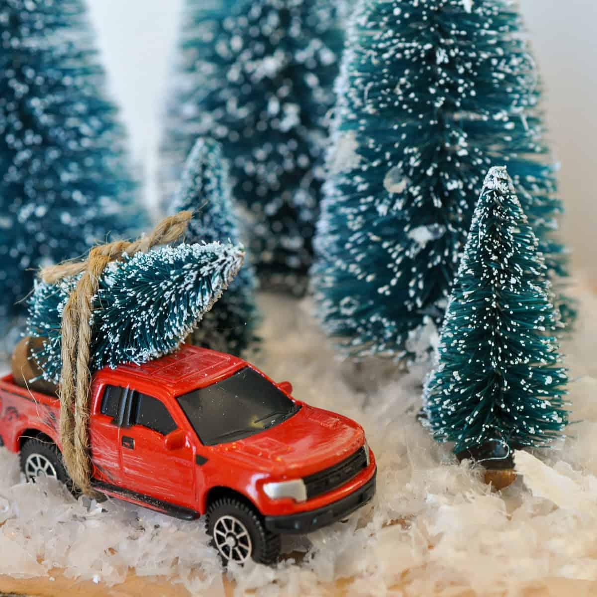 Red Christmas toy truck with bottle brush Christmas tree tied on the back.