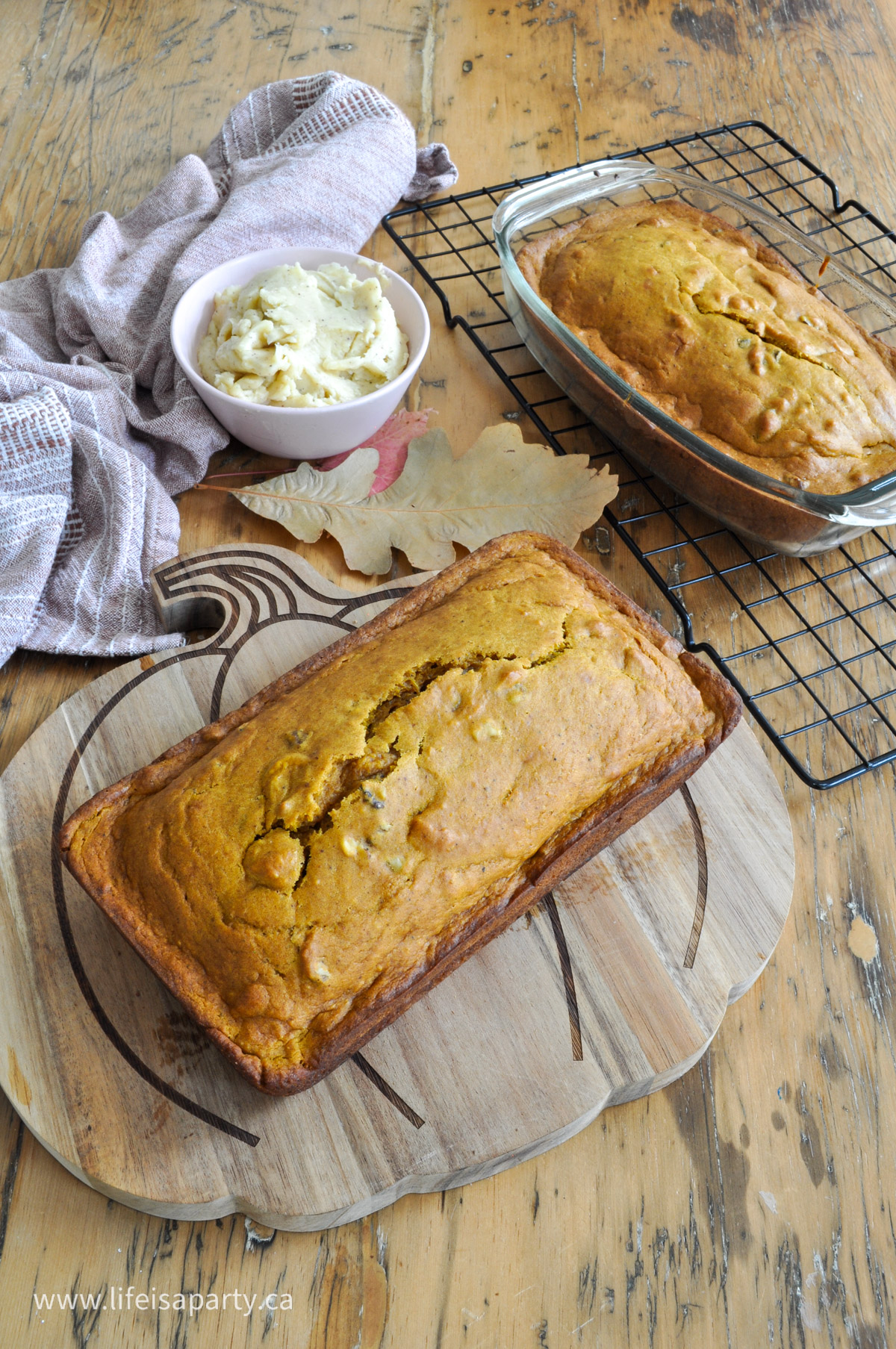 Two loaves of ginger pumpkin loaf, one on a cutting board and one on a cooling rack beside a bowl of cinnamon honey butter.