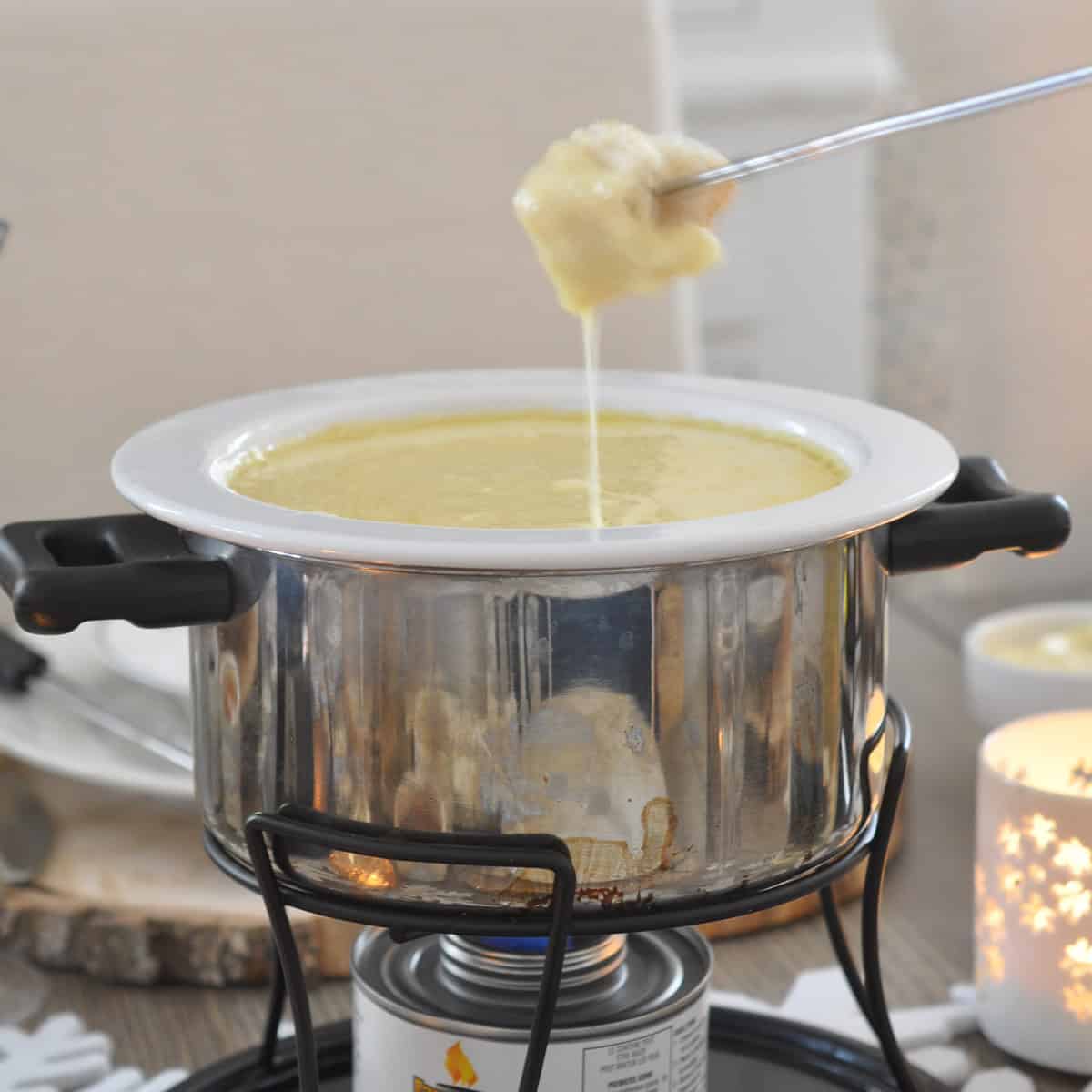 Cheese fondue in a fondue pot with a bread dipper dripping with cheese.